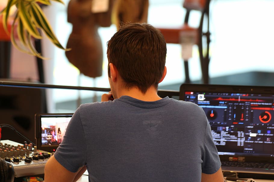 man sitting in front of turned-on laptops with DJ mixer applications HD wallpaper