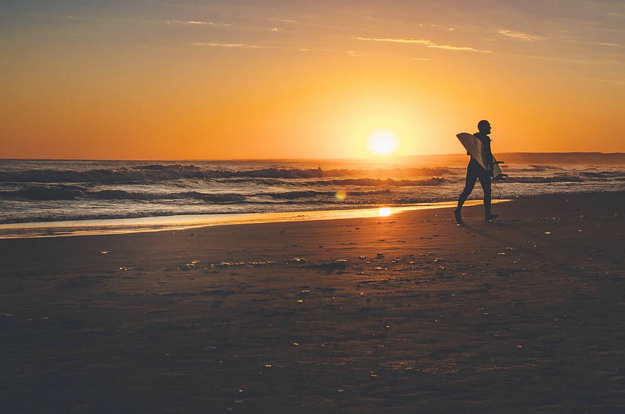man about to walk on seashore during golden hour, silhouette photograph of person waling on beach with surfboard HD wallpaper