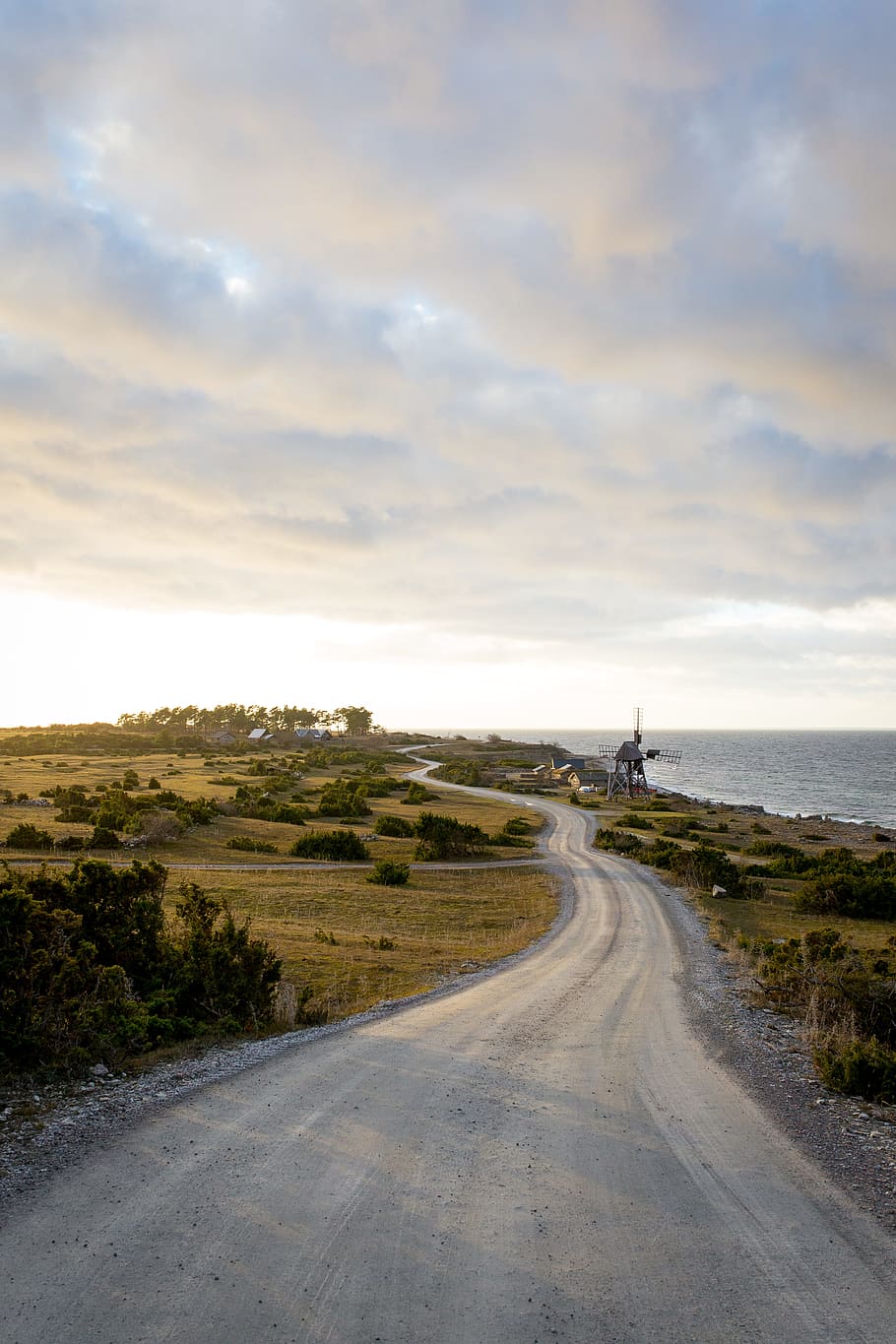 curved road surrounded by grass lawn, photo of rough road near body of water HD wallpaper