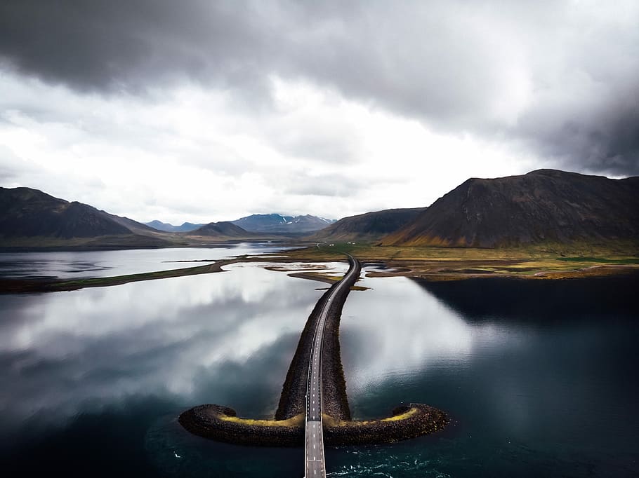 asphalt road in the middle of bodies of water, road bridge near mountains under cloudy sky HD wallpaper