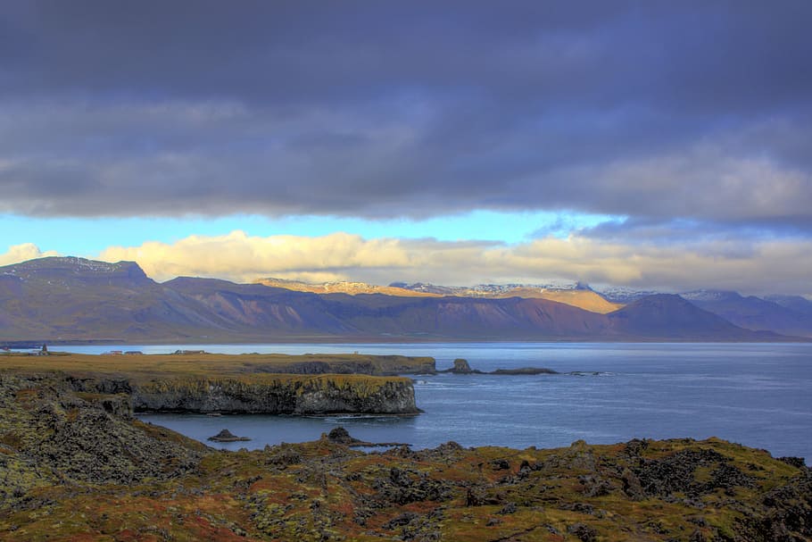 green land beside a body of water, mountain near sea in distant of other mountain under cloudy sky HD wallpaper