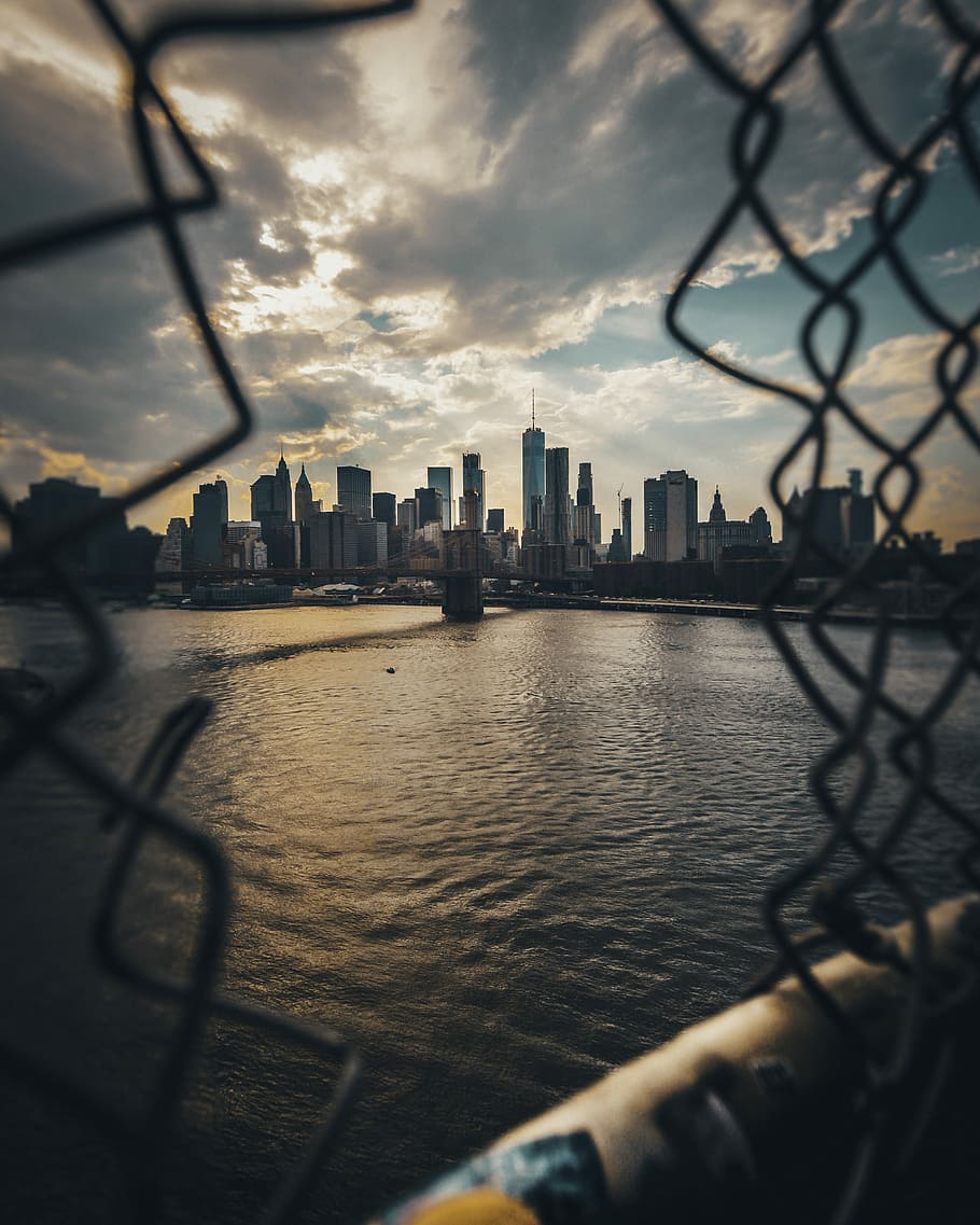 gray fence overlooking body of water far at the city, New York skyline showing Brooklyn bridge