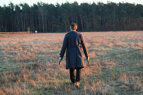 man holding two guns and walking on grass field during daytime HD wallpaper