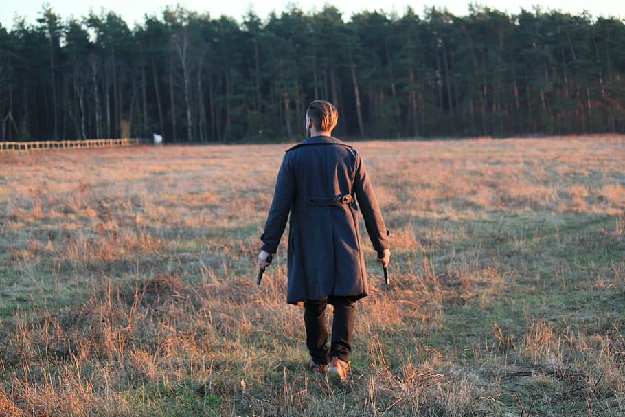 man holding two guns and walking on grass field during daytime HD wallpaper