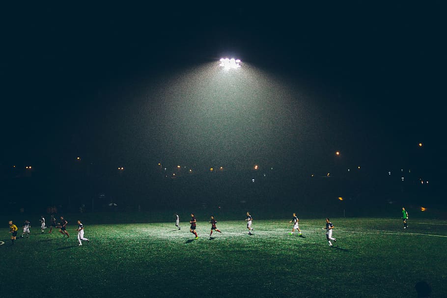 group of people playing soccer on soccer field, photo of soccer players playing during nighttime