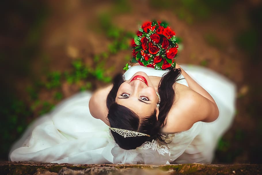 shallow depth of fields photography of woman wearing wedding dress while holding bouquet of roses