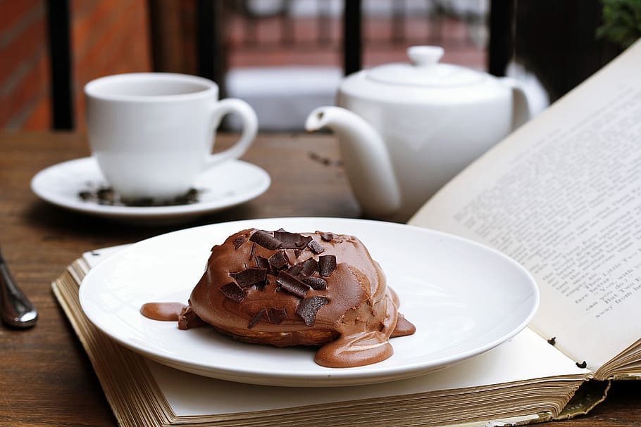 Chocolate dessert on an open book with a tea pot and tea cup in the background, photo of chocolate pastry in serving plate on book HD wallpaper