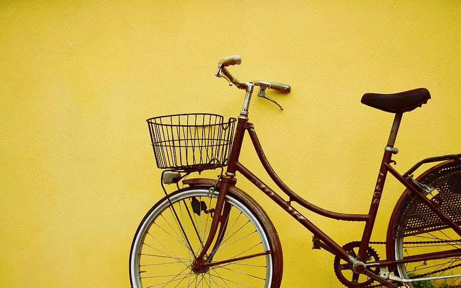 female beach cruiser bike leaning on yellow painted wall, brown female beach cruiser bike park beside yellow wall