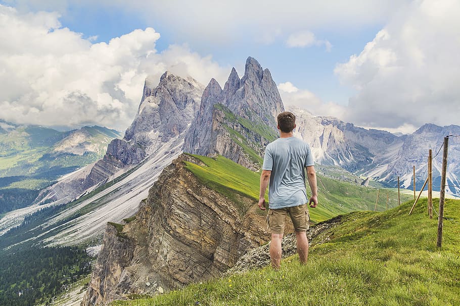 man in blue T-shirt on top of the mountain under the blue sky, man standing near top of mountain during daytime, HD wallpaper