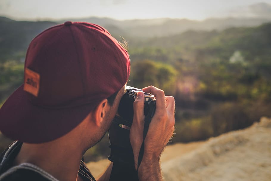 man in red fitted cap taking picture, photo of person taking photos on mountain range HD wallpaper