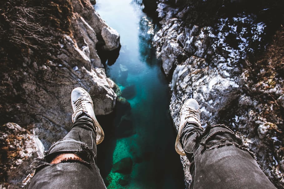 man sitting on edge of cliff looking on body of water during daytime HD wallpaper