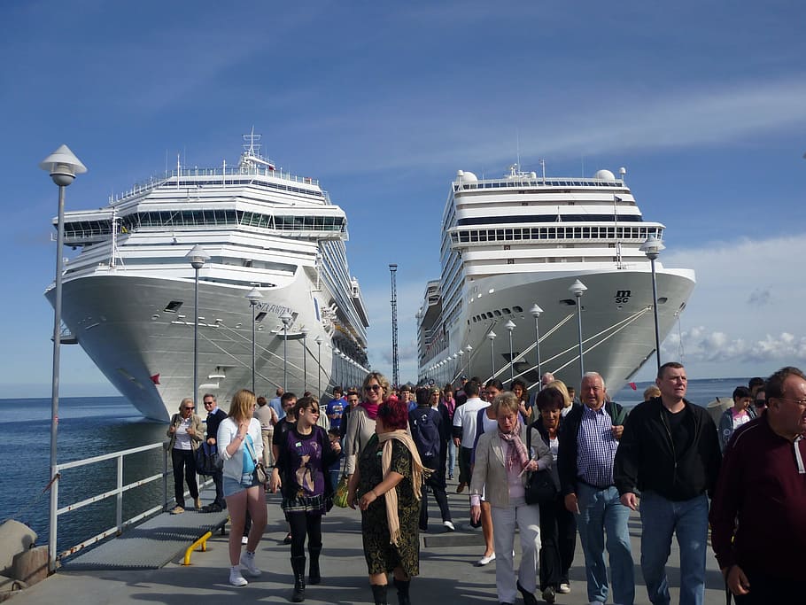 people walking on gray dock between two white cruise ships during daytime