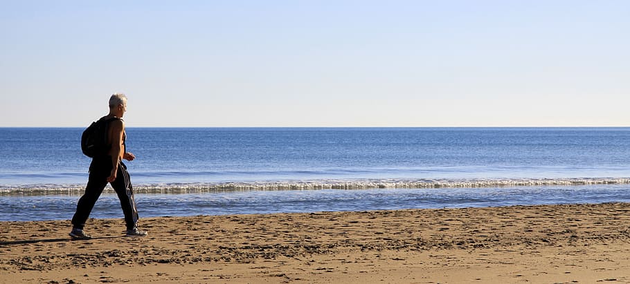 man walking beside body of water under blue and white sky during daytime HD wallpaper