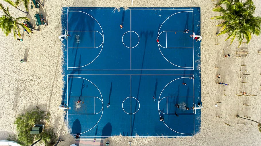 aerial photography of basketball court, aerial view of blue basketball court in the middle of sand with coconut trees