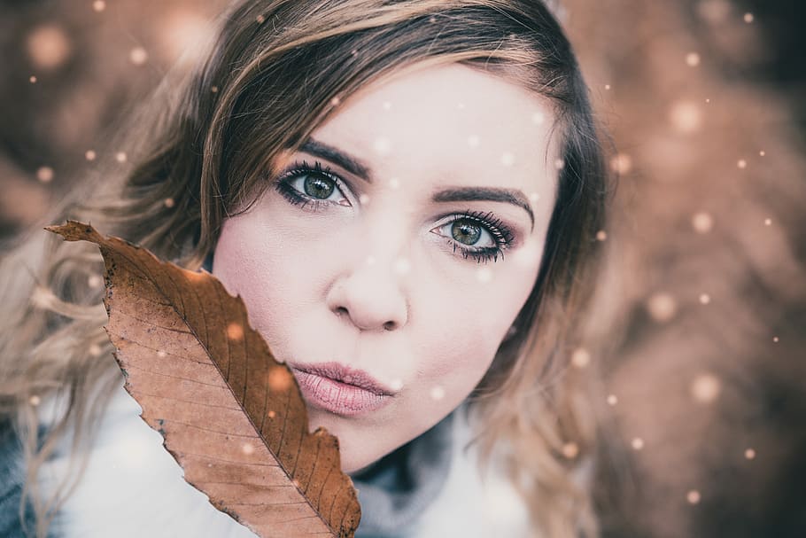 selective focus photo of woman holding brown leaf, woman's face and brown dried leaf HD wallpaper