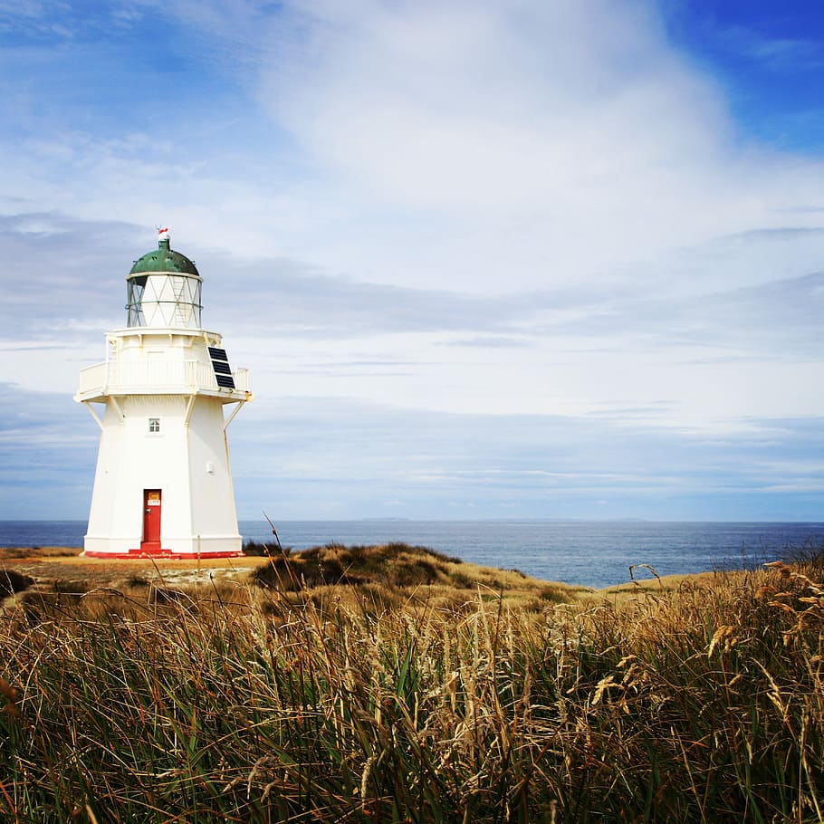 photo of white concrete lighthouse near ocean under blue cloudy sky, white lighthouse on cliff under blue sky HD wallpaper