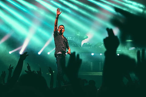 man in black and gray button-up collared shirt standing on stage with green lights turned on, man raising his right hand over crowd of people HD wallpaper