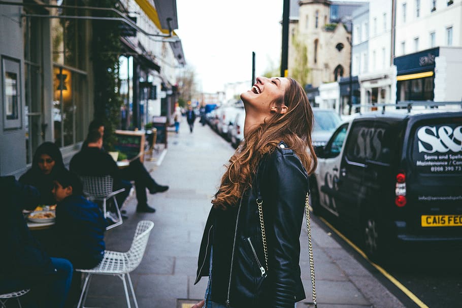 Unbridled Joy, woman in black leather jacket laughing on road side near cars parked on gray asphalt road during daytime