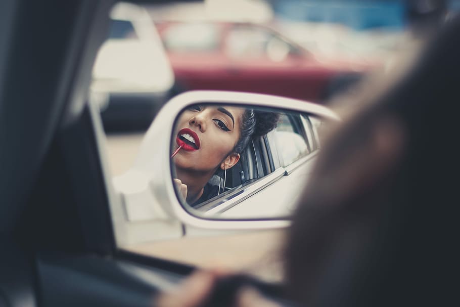 woman putting liquid lipstick on her lips while looking at vehicle's mirror during daytime, selective focus photography of vehicle side mirror reflecting woman in red lipstick HD wallpaper