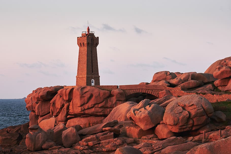 brown lighthouse on rock cliff near body of water, gray tower near cliff on body of water HD wallpaper