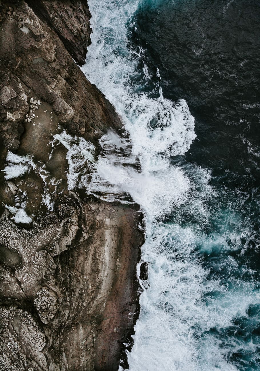 bird's eye view water waves crashing to rocks, body of water beside brown mountain HD wallpaper