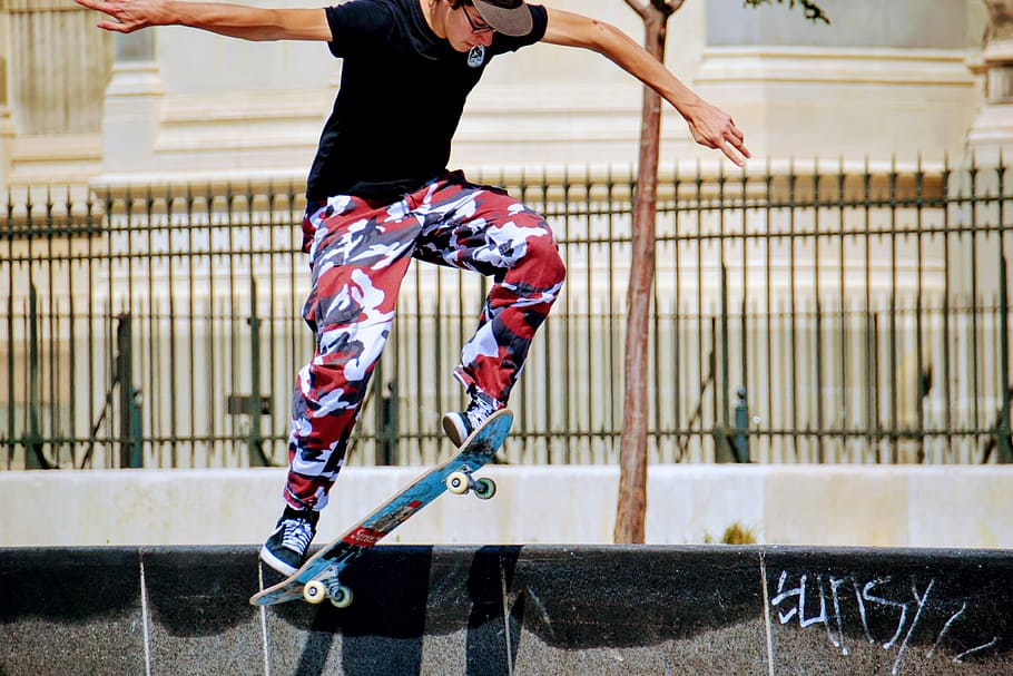 man on skateboard photo, photo of man wearing black shirt and red-and-white pants skateboarding along street HD wallpaper