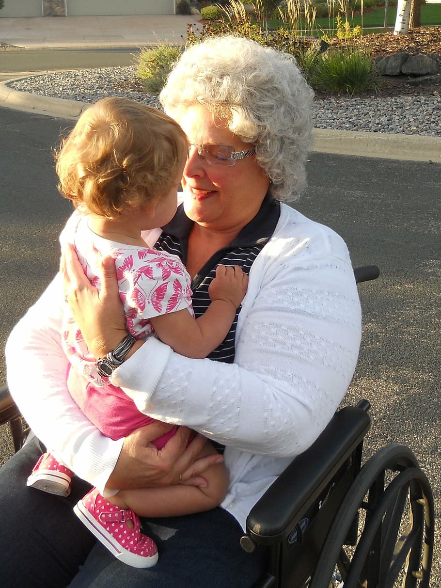 woman sitting on wheelchair carrying girl, grandma, granddaughter