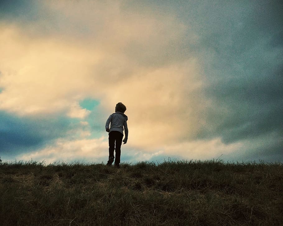 person in gray hoodie and black pants standing on green grass under blue cloudy skies HD wallpaper