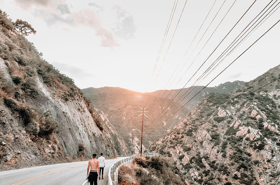 man in black shorts walking on gray road, photo of two people walking on concrete road towards mountains HD wallpaper