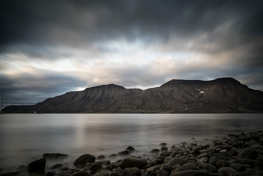 mountain near ocean during daytime, rippling body of water near rocks HD wallpaper