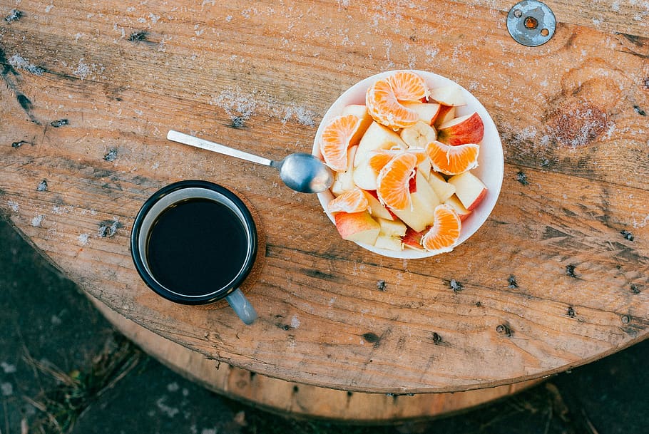 orange and apple on bowl, sliced oranges and apples inside round white ceramic bowl with silver spoon on top beside black ceramic mug HD wallpaper