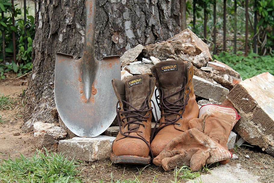 pair of brown boots and black shovel beside some piles of rocks HD wallpaper