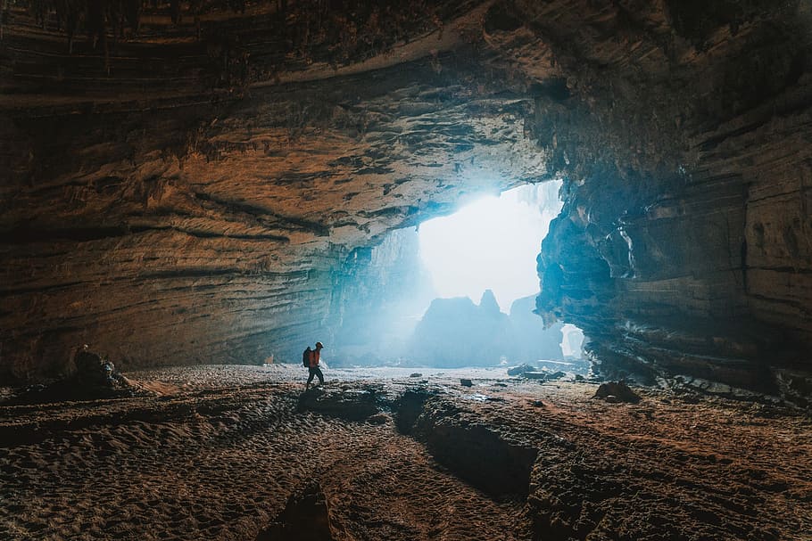 person walking towards cave, man walking inside the cave during daytime
