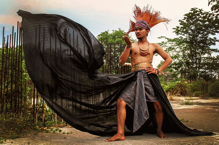 man wearing black and gray shorts and orange headdress, man wearing black floor length with headrest standing near brown wood cage at daytime HD wallpaper