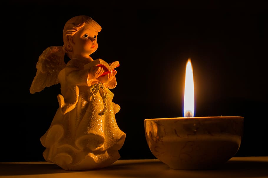angel holding book figurine beside lighted candle, prayer, vera