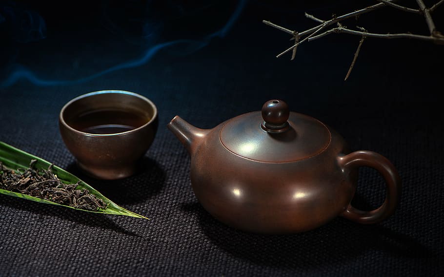 brown teapot near cup on black surface, still life photography