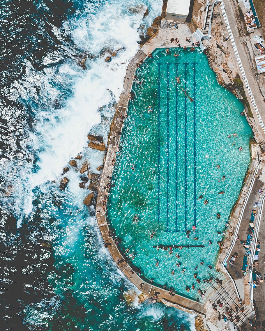 aerial view of beach and pool, aerial photography of people swimming near pool beside seashore during daytime HD wallpaper