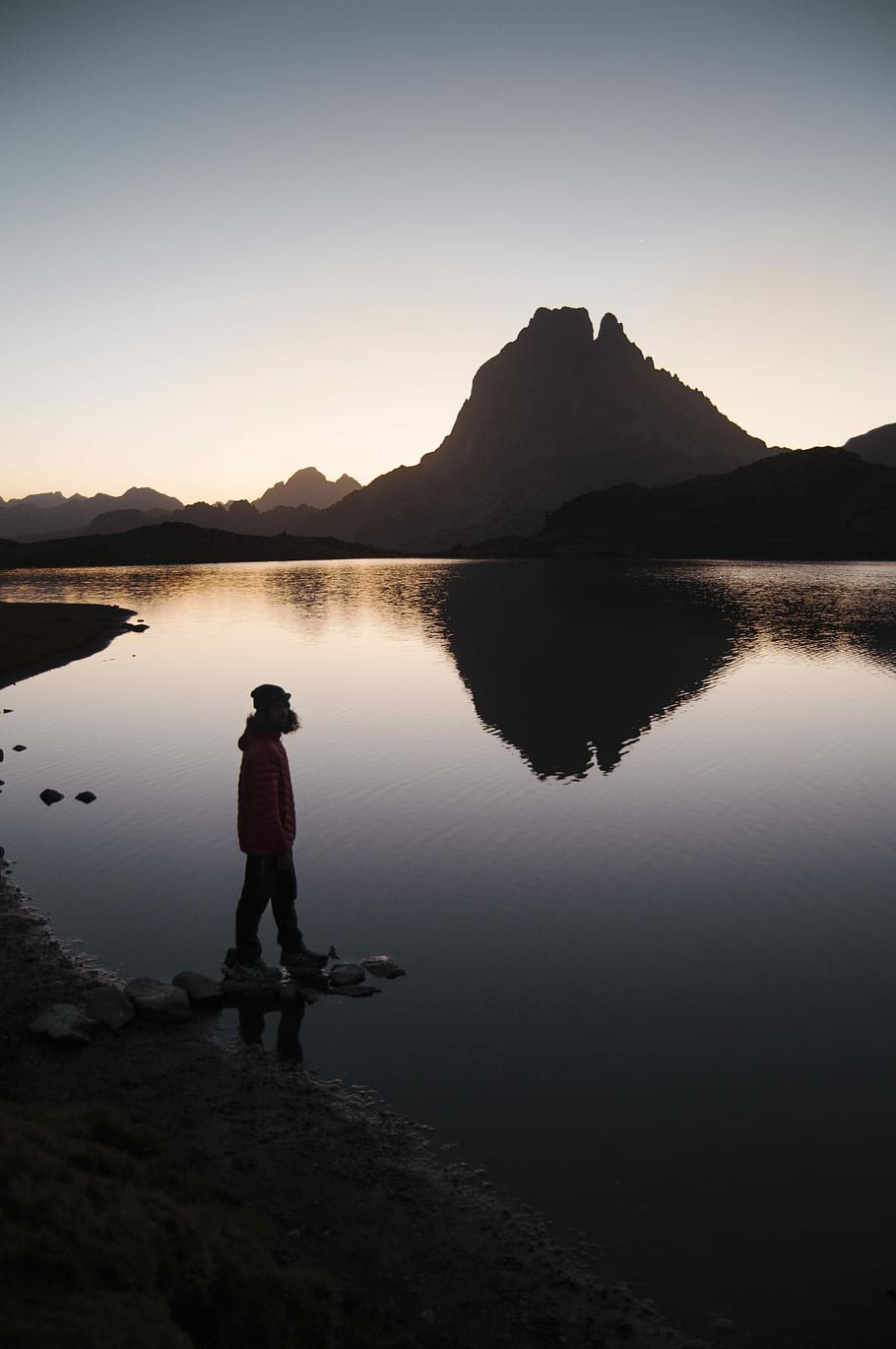 silhouette of person standing beside body of water near mountain during golden hour, man standing far away from island