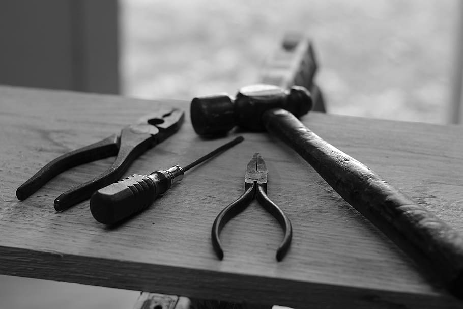 four handheld tools on board, grayscale photo of pliers, screwdriver, and hammer