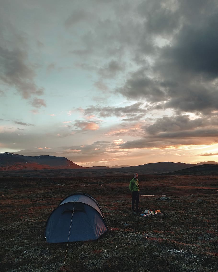 man in green jacket, person standing near blue dome tent during daytime HD wallpaper