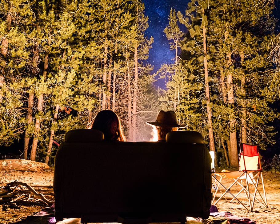 two people sitting in front of bonfire in forest at nighttime HD wallpaper