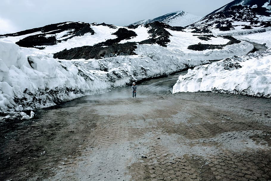 person standing near snow caps mountain, boy standing in the middle of the road during winter and day HD wallpaper