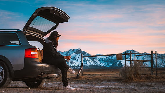 man sitting on car's tail looking at ranch, person sitting at the back of the car looking at the mountain HD wallpaper