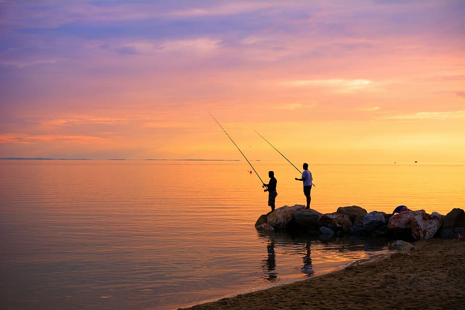 two men fishing standing on stones, aegean sea, back lit, color image