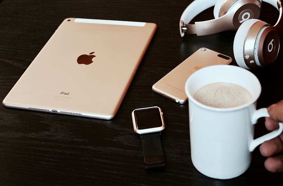 person holding white ceramic mug near silver iPad, cafe, apple