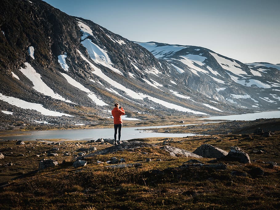 person standing on rock near body of water and mountain, person standing on grass near body of water and snowcapped mountain HD wallpaper