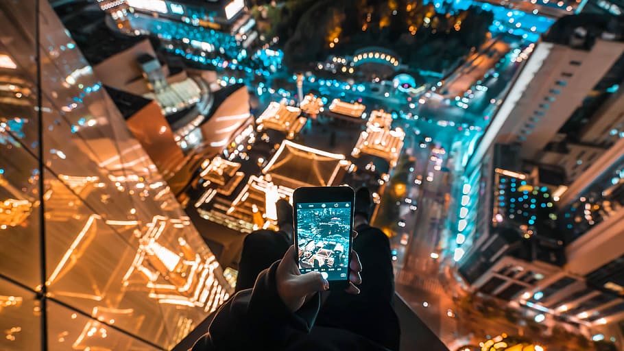 person on skyscraper taking a photo of building below during nighttime, person holding black smartphone displaying camera HD wallpaper