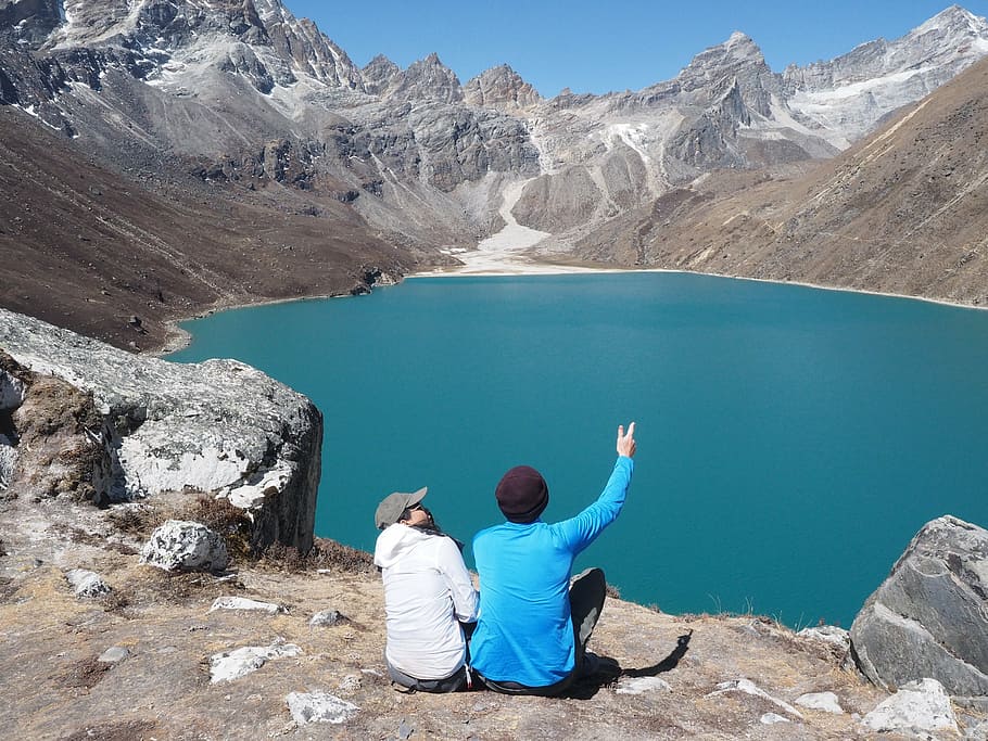 two person sitting in front of blue water, gokyo, lake, nepal