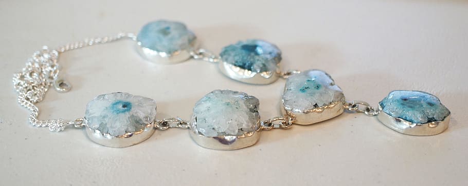 silver-colored teal stone necklace on white board, solar quartz geode