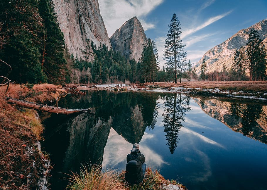 person sitting on rock looking at body of water near forest during daytime, body of water surrounded by rocky mountains during daytime photography, HD wallpaper